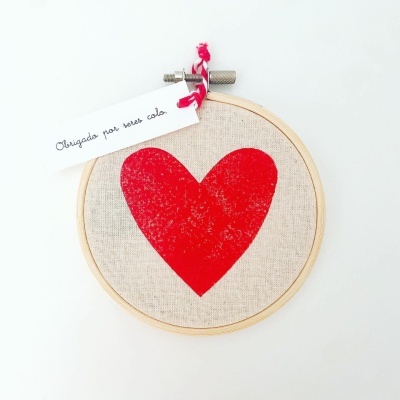 Bastidor com coração vermelho em tecido bege e etiqueta com texto