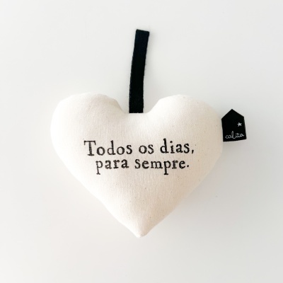 Almofada em tecido bege em forma de coração com texto em preto e fio para pendurar