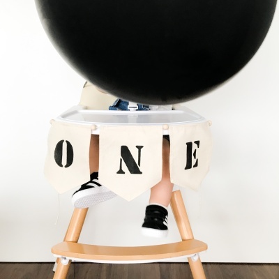 Cadeira alta decorada com faixa 'ONE' e balão preto