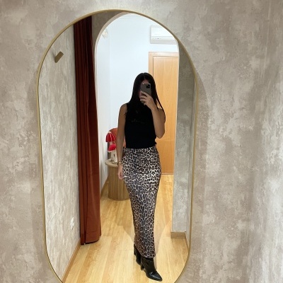 Mulher com top preto e saia animal print a tirar selfie num espelho redondo com moldura dourada