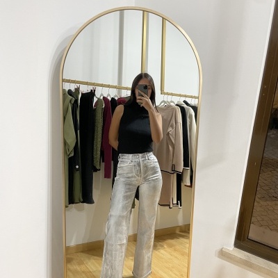 Mulher numa selfie em espelho com roupa preta e calças cinza claro largas, arara de roupas ao fundo