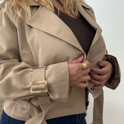 Casaco bege com cinto e fivela usado com camisola castanha e calças de ganga azuis