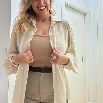 Mulher com camisa bege transparente, camisola bege e calças bege em ambiente interior