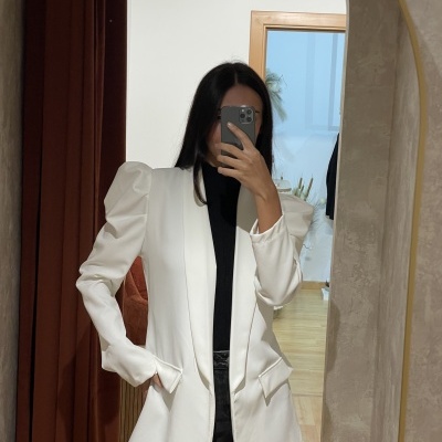 Pessoa a tirar selfie num espelho usando blazer branco estruturado e roupa preta e cinza