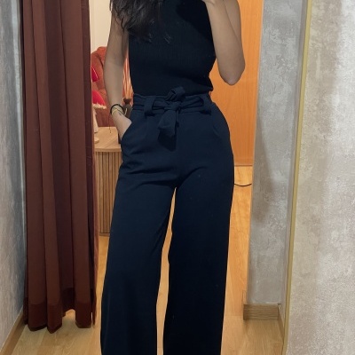 Calças pretas de tecido fluído com cinto e top canelado preto em ambiente interior