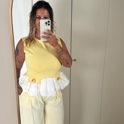 Pessoa com top amarelo e calças amarelas claras em frente a um espelho