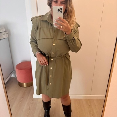 Vestido verde com botões dourados e botas pretas em ambiente interior claro