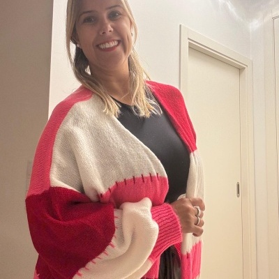 Cardigan de malha vermelho, branco e rosa em mulher sorridente com cabelo loiro, em ambiente interior claro.