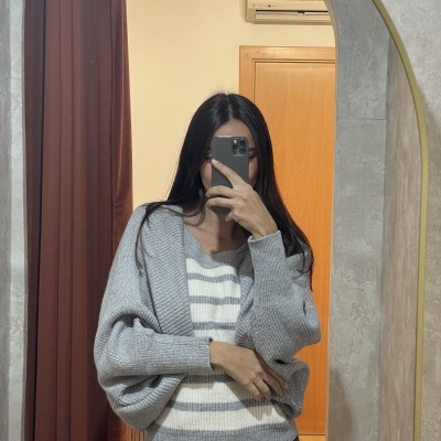 Mulher com cardigan cinzento e camisola de riscas a tirar selfie num espelho