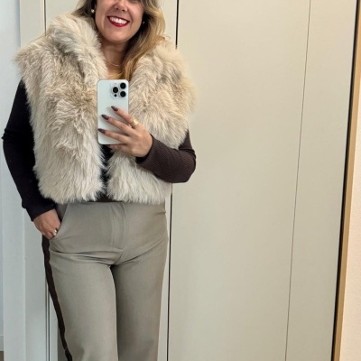 Mulher com colete de pelo bege e calças bege em selfie na casa