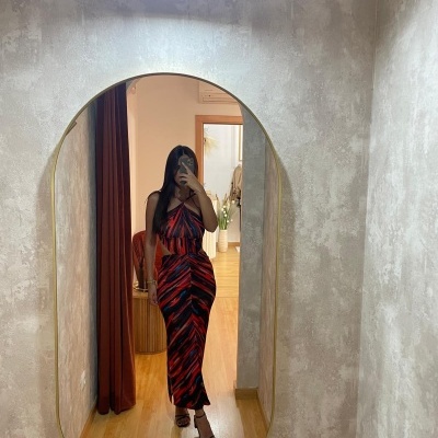 Mulher com vestido longo às riscas vermelhas e pretas a tirar selfie ao espelho oval com moldura dourada