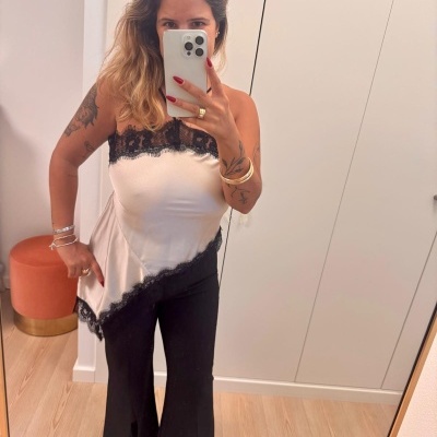 mulher com top de cetim bege e renda preta, calças pretas, selfie em espelho