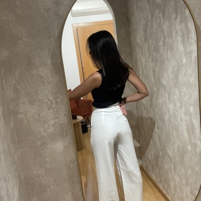 Calças largas brancas com cinto refletidas num espelho oval numa parede cinzenta