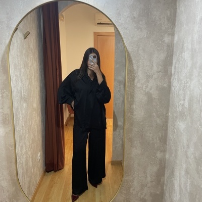 espelho oval dourado na parede cinzenta refletindo pessoa com roupa preta e sapatos vermelhos