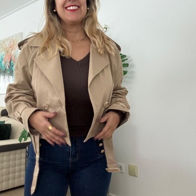 mulher com casaco bege curto, blusa castanha e jeans azul em sala