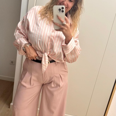 Mulher com camisa rosa às riscas brancas e calças rosa largas a tirar selfie