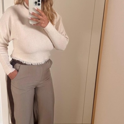 Mulher com camisola creme de malha e calças castanhas largas com risca lateral em espelho.