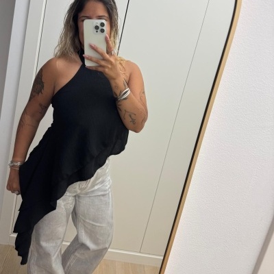 Pessoa com top preto assimétrico e calças largas de ganga claras a tirar selfie num espelho