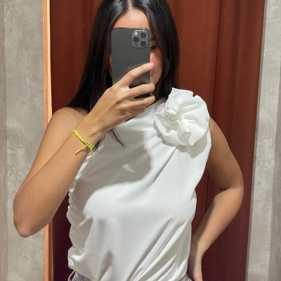 Mulher a tirar selfie no espelho com blusa branca sem mangas com flor grande no ombro