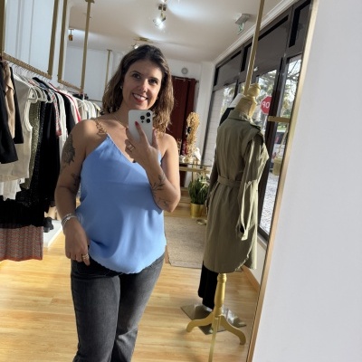 Mulher com camisola azul clara e calças pretas num ambiente de loja com manequim e araras de roupa