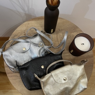 Carteiras pequenas preto, prata e dourado sobre mesa de madeira com vaso e vela castanhos