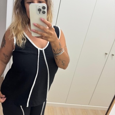 Mulher com conjunto preto e riscas brancas a tirar selfie em espelho com telemóvel