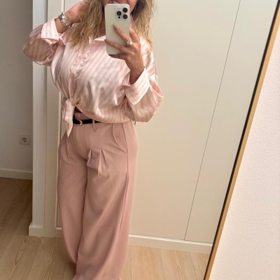 Mulher com camisa de riscas rosa e branca e calças rosa claro em selfie no espelho