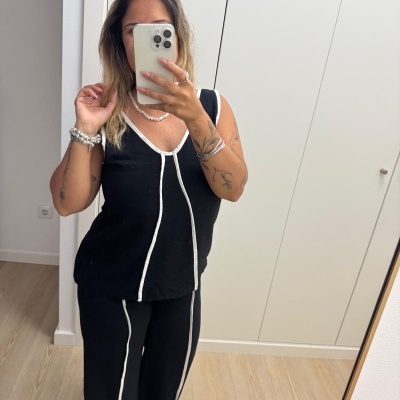 Mulher a tirar selfie em espelho usando conjunto preto com detalhes brancos em divisão com chão de madeira clara