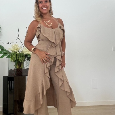 Mulher vestindo conjunto bege com vestido de babados e calças largas, em ambiente interno claro.