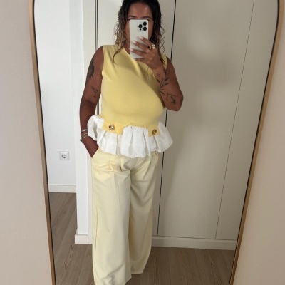 Mulher a tirar selfie em espelho com top amarelo com aplicação branca na cintura e calças largas amarelo claro.