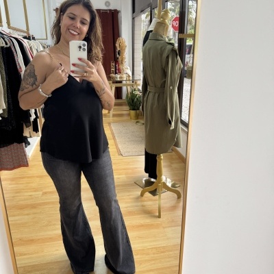 mulher com top preto e calças jeans num espelho dentro de loja com manequim e casaco verde