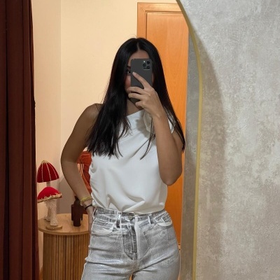 Pessoa a tirar selfie no espelho com camisola branca e calças de ganga cinzentas claras