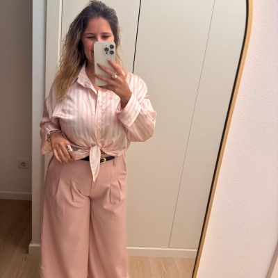 Mulher a tirar selfie num espelho com camisa às riscas rosa e branca e calças largas rosa claro