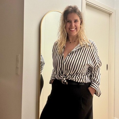 Mulher com blusa de riscas verticais preta e branca e calças pretas junto a espelho