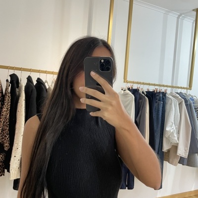 Mulher com camisola preta canelada frente a espelho em loja de roupa