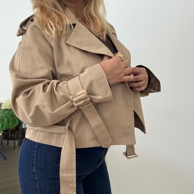 Casaco bege curto com cinto usado por mulher em ambiente interior