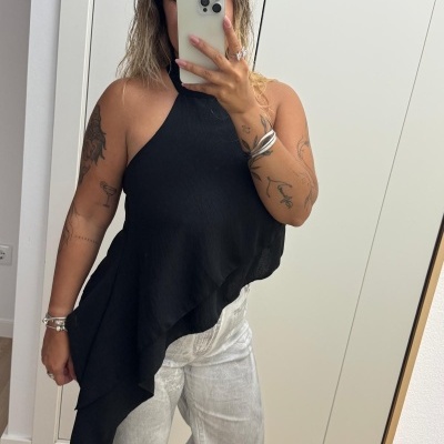 Pessoa com blusa preta assimétrica e calças cinza clara num espelho