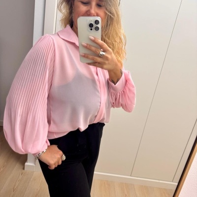 Mulher com camisa rosa e calças pretas a tirar selfie em espelho