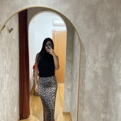 Mulher com saia comprida de padrão cebra e top preto em espelho grande com moldura dourada