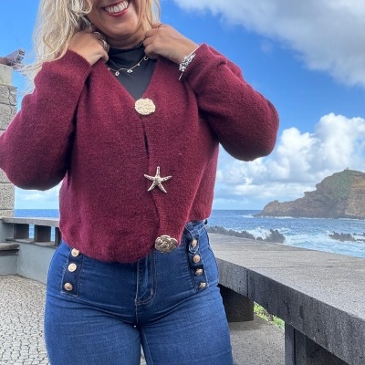 Mulher com casaco vermelho de malha e calças de ganga azuis junto ao mar