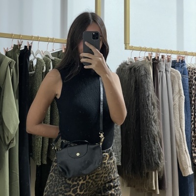 Pessoa com top preto e calças animal print numa loja com várias roupas penduradas ao fundo