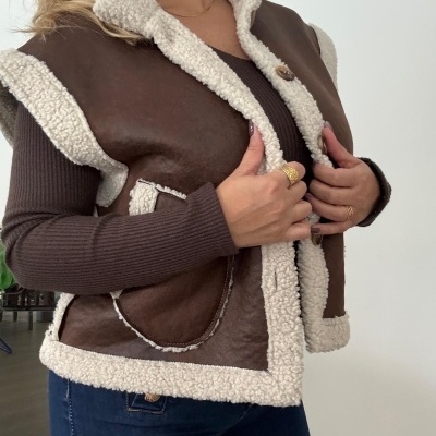 Colete castanho em pele com forro creme e mulher a usar com camisa castanha e jeans azul.