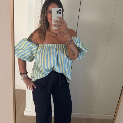 Mulher com blusa às riscas azuis e amarelas e calças pretas largas a tirar selfie no espelho