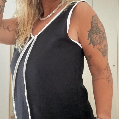 Blusa preta sem mangas com acabamento branco usada por mulher com acessórios e tatuagens