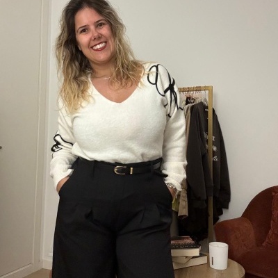 Mulher com camisola branca e calças pretas na sala com cabide e mesa