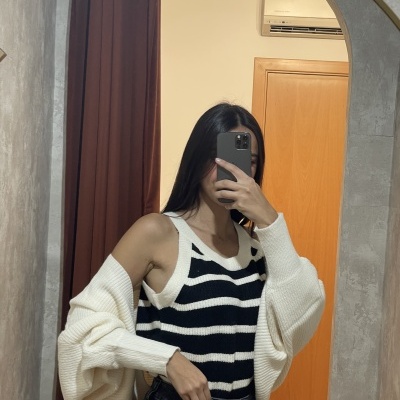 Top de malha riscas pretas e brancas com casaco de malha branco num espelho com moldura curva e parede com porta de madeira