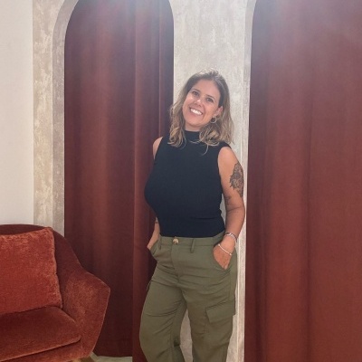 Mulher com camisola preta e calças cargo verde-oliva em frente a cortinas castanhas