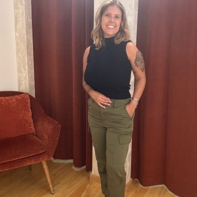 Mulher sorridente com calças cargo verdes e camisola preta sem mangas em ambiente interior