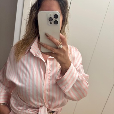 Camisa riscada rosa e branca com nó combinada com calças rosa e cinto preto num espelho.