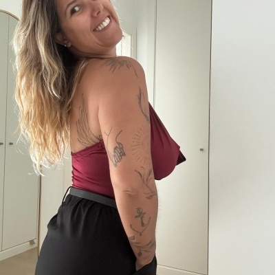 Mulher com top borgonha e calças pretas num quarto com armário branco